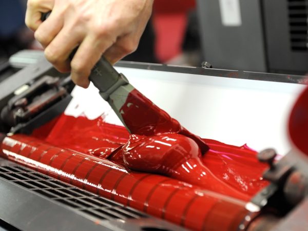 Worker uses specialized spatula to apply red paint to industrial printer